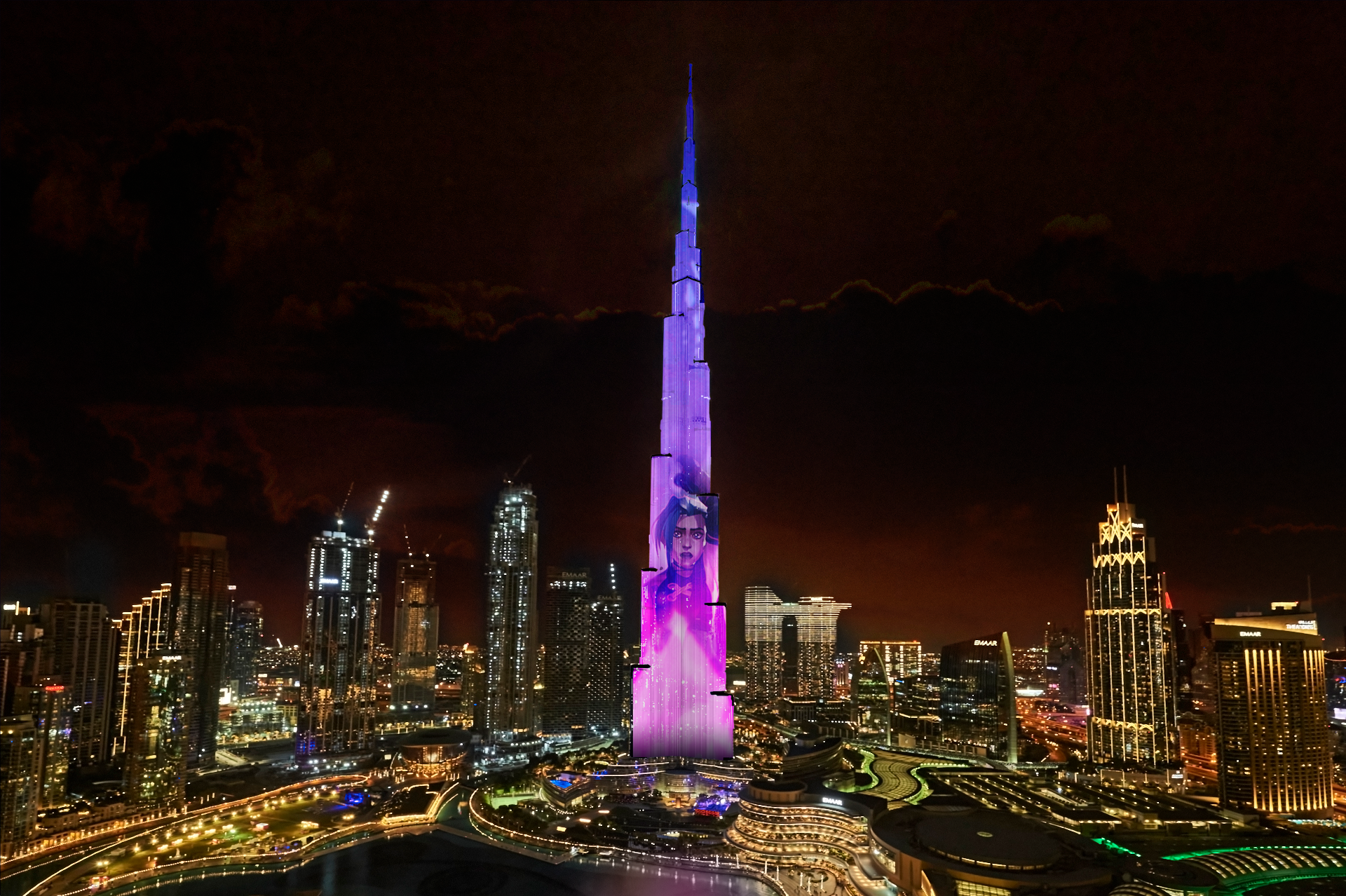 The Burj Khalifa in Dubai is illuminated at night with vibrant lights and a large projected image of a woman’s face, reminiscent of Netflix Arcane style, surrounded by city skyscrapers and glowing streetlights.