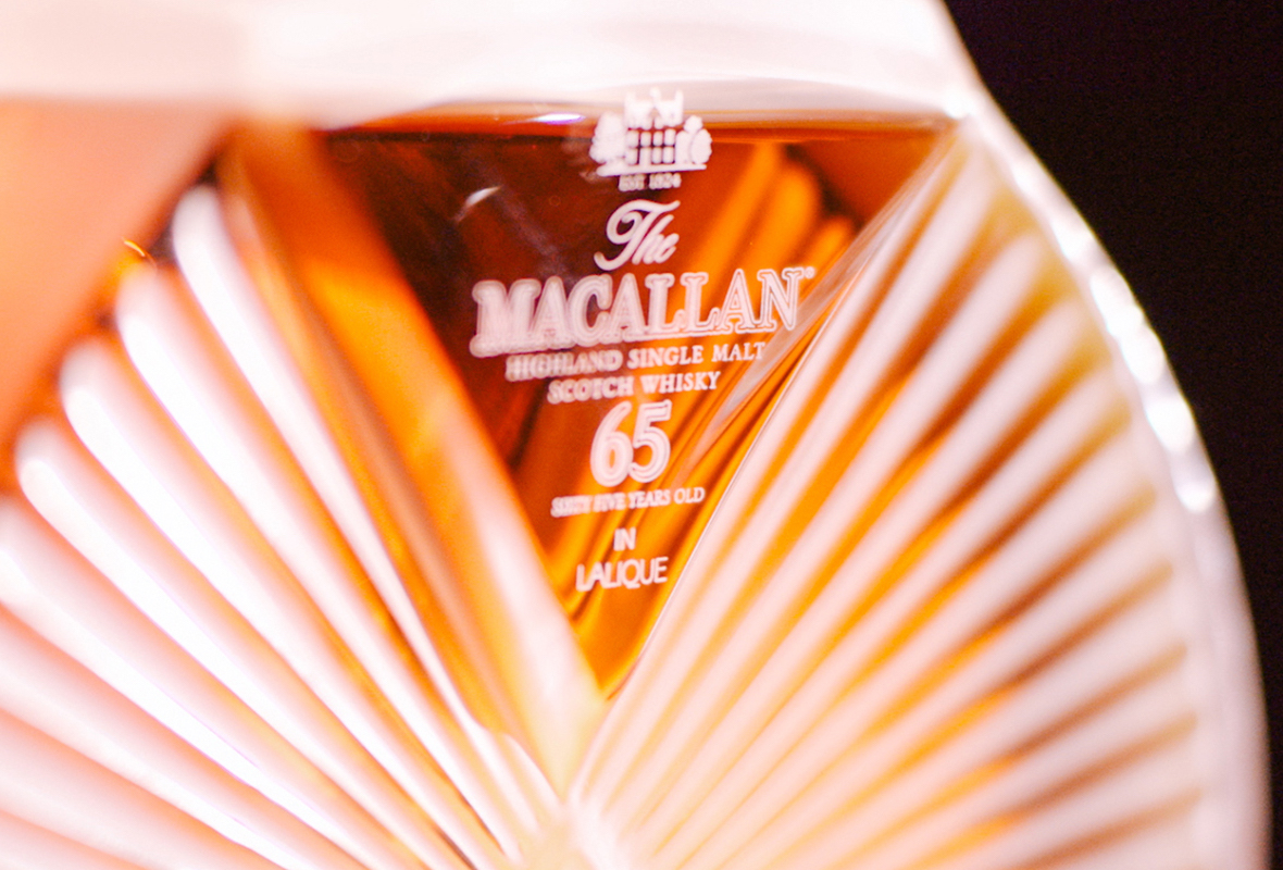 Close-up of a bottle of The Macallan 65 Years Old Highland Single Malt Scotch Whisky in a decorative Lalique decanter, golden amber liquid visible inside—an iconic highlight in any The Macallan case study.