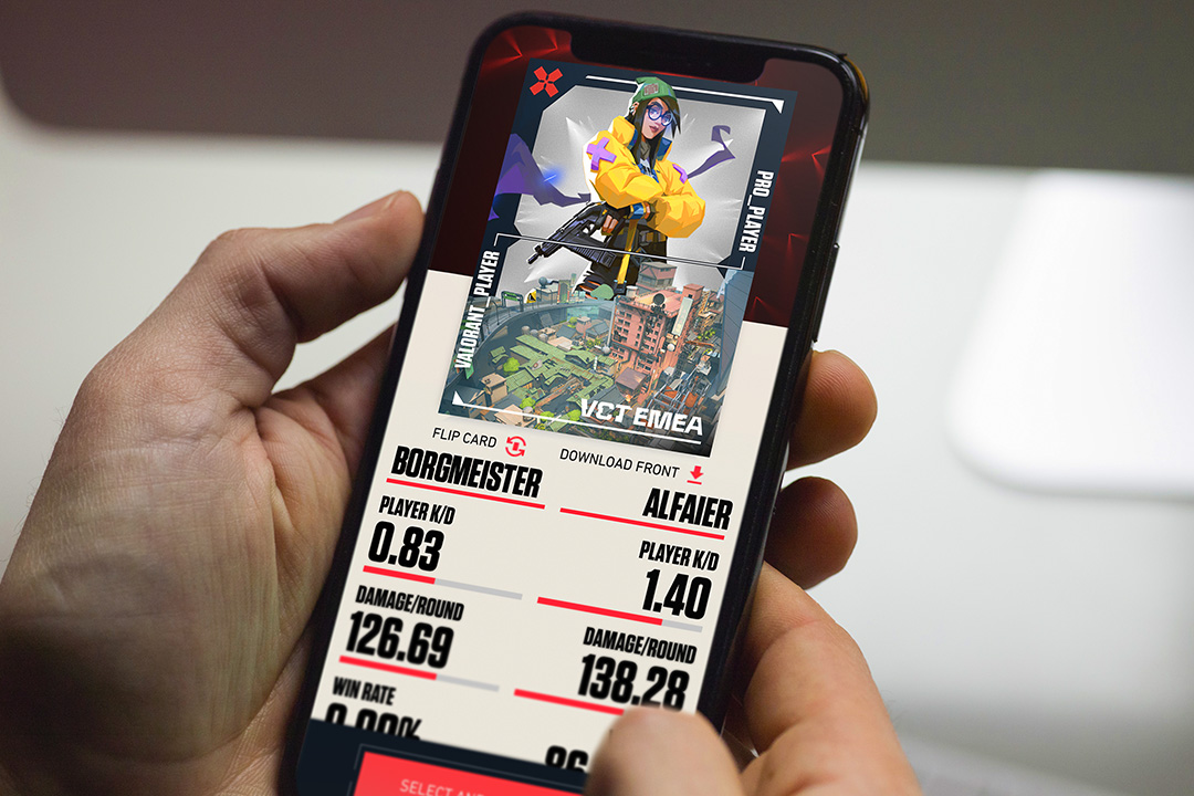 A person holds a smartphone displaying a Riot Games VCT gaming stats comparison for two Valorant players, showing character images, player names, win rates, kill/death ratios, and damage per round.
