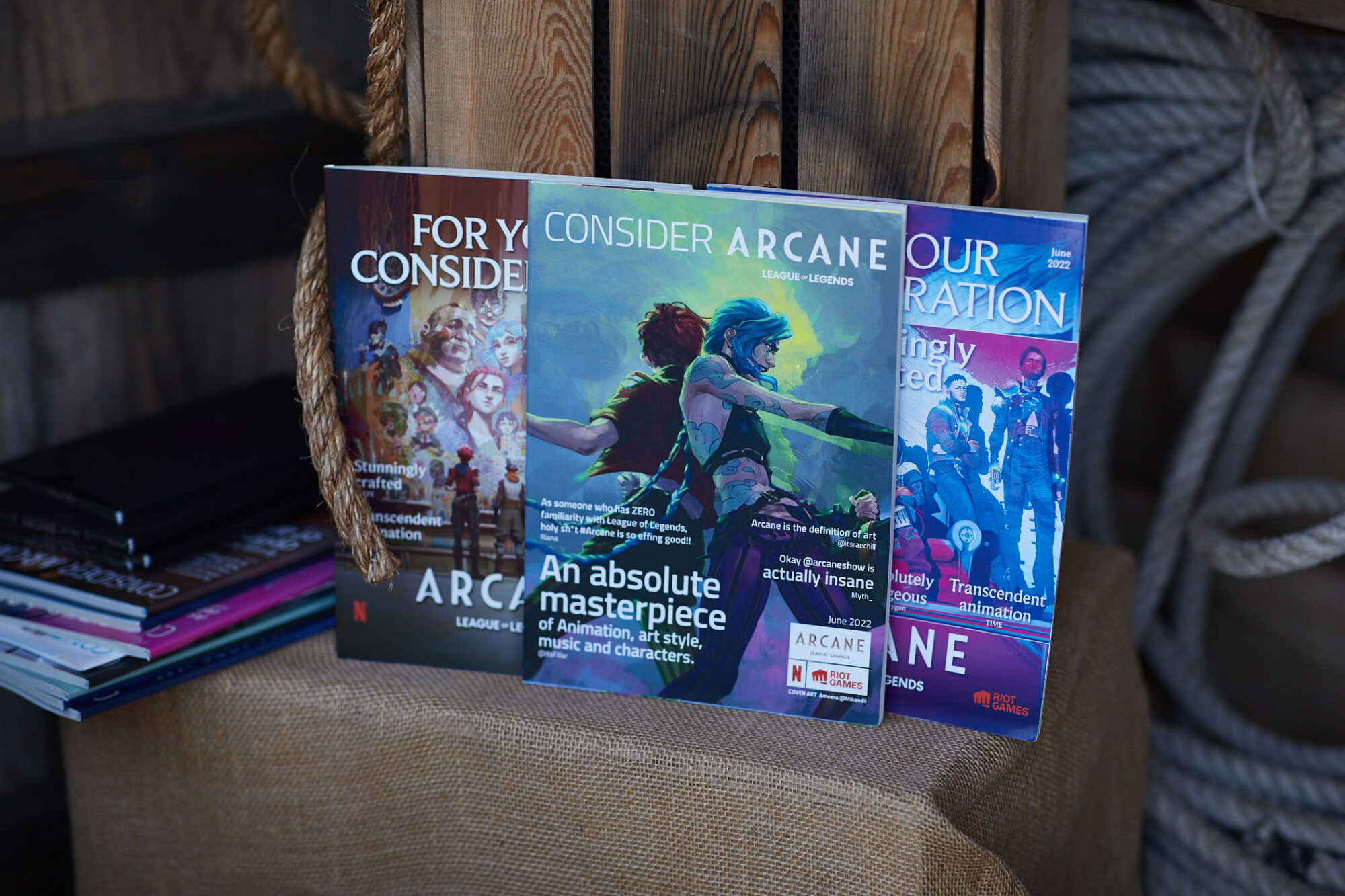 Three colorful Arcane FYC Emmys promotional magazines are displayed upright on a burlap-covered surface next to thick rope. Each features cover art and text highlighting the animation, story, and characters of the show.