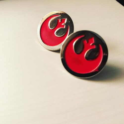 Two round cufflinks featuring the red Rebel Alliance symbol from Star Wars on a white surface. Perfect for a marketing team aiming to showcase their fandom, these cufflinks have a metallic edge and are positioned at an angle, with one closer to the camera.