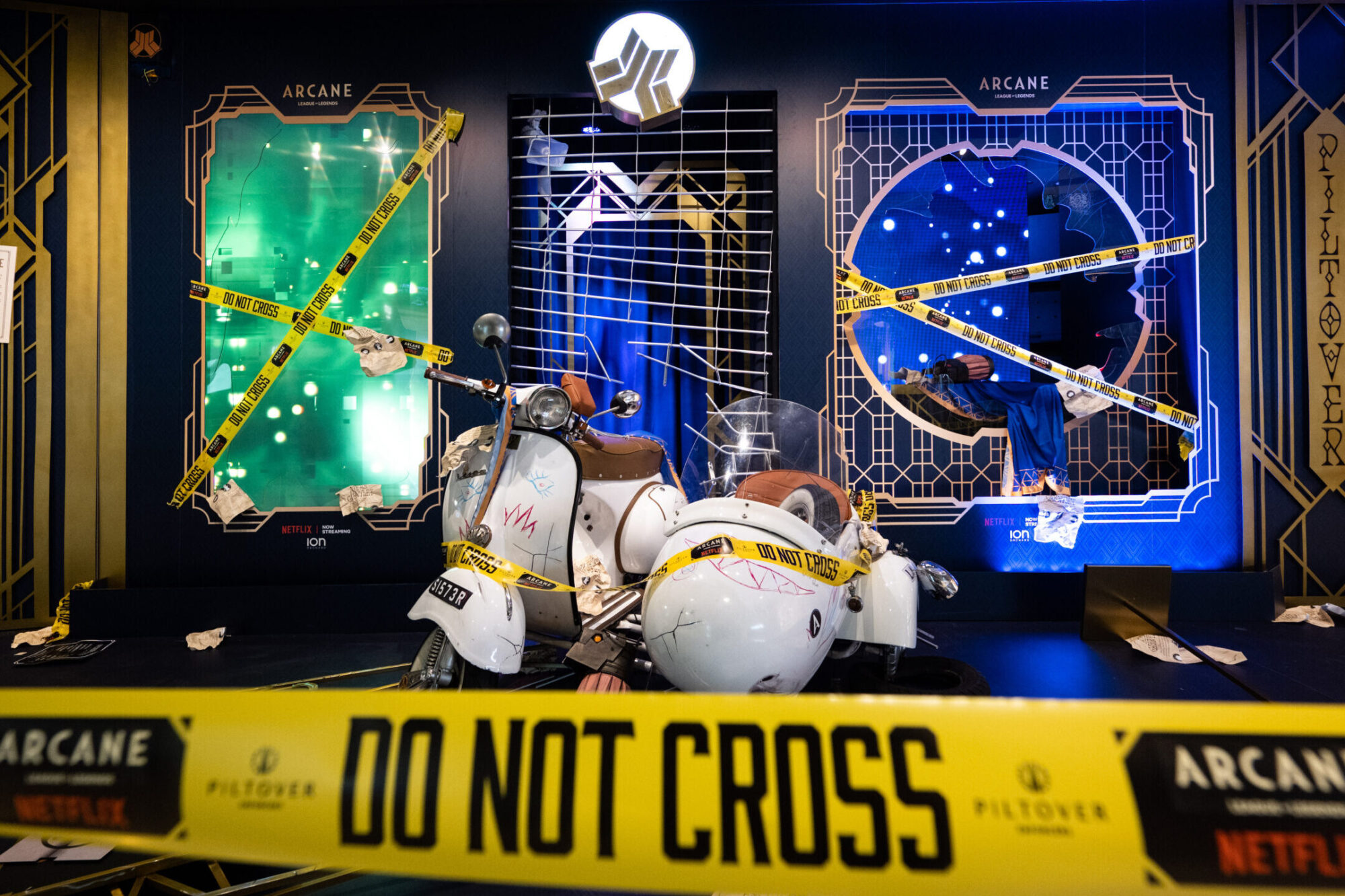 A white scooter crashes through a display with yellow DO NOT CROSS tape, broken glass panels, and Netflix Arcane signage in the background, creating a dramatic crime scene exhibit.