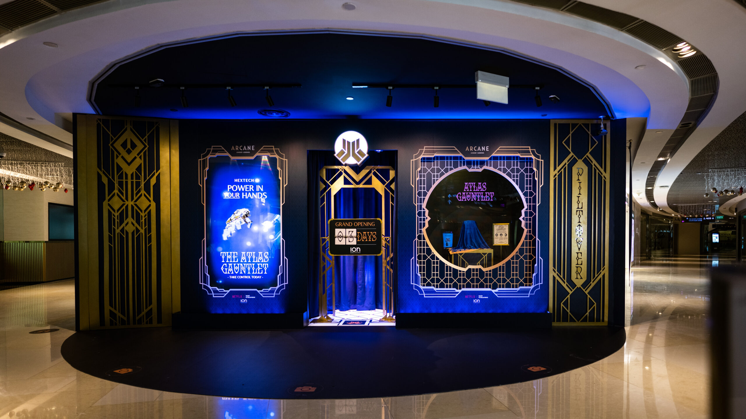 A decorative, art-deco themed display with glowing blue and gold lights stands in a mall. Large posters promote Netflix Arcane and a QR code is displayed at the center, with mirrors reflecting the surroundings.