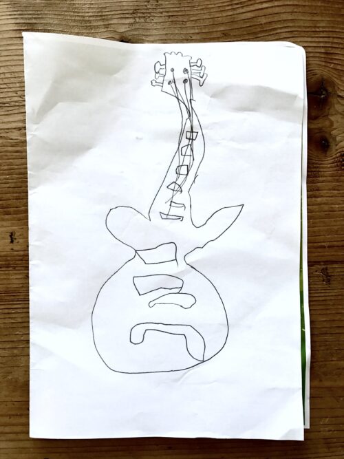 A child’s drawing of a guitar in black marker on white paper, with abstract lines and shapes, placed on a wooden surface—perfect inspiration for a creative marketing team.