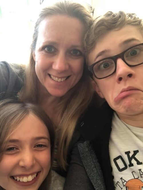 A woman and two children pose for a selfie. The woman and girl are smiling, while the boy, wearing glasses, makes a silly face. Like a playful marketing team, all three huddle close together and look straight at the camera.
