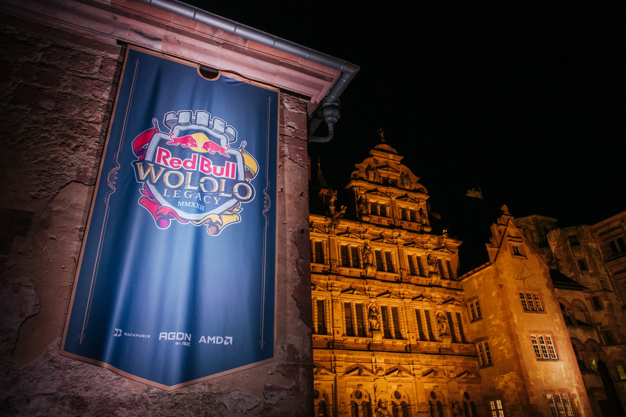 A large Red Bull Wololo: Legacy banner hangs on an exterior wall at night, with a historic, ornately lit building in the background.