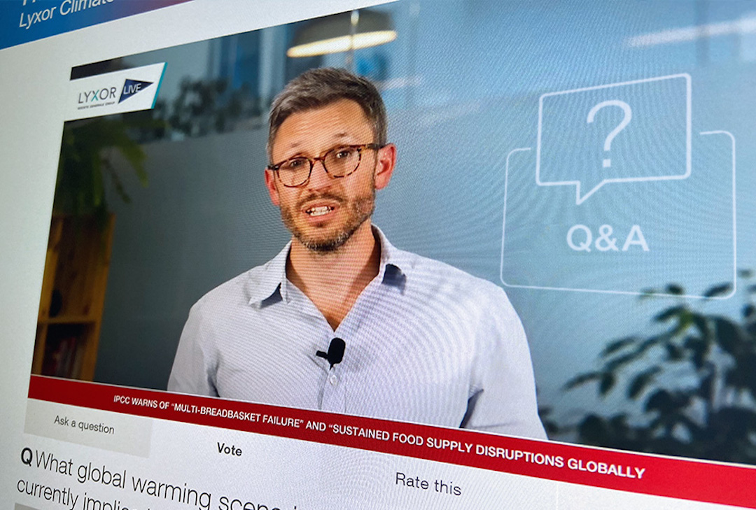 A man wearing glasses and a blue shirt speaks in front of a camera during an online Q&A session featuring a Lyxor ETF case study, with the screen displaying a Q&A icon, text, and a news ticker about global food supply disruptions.