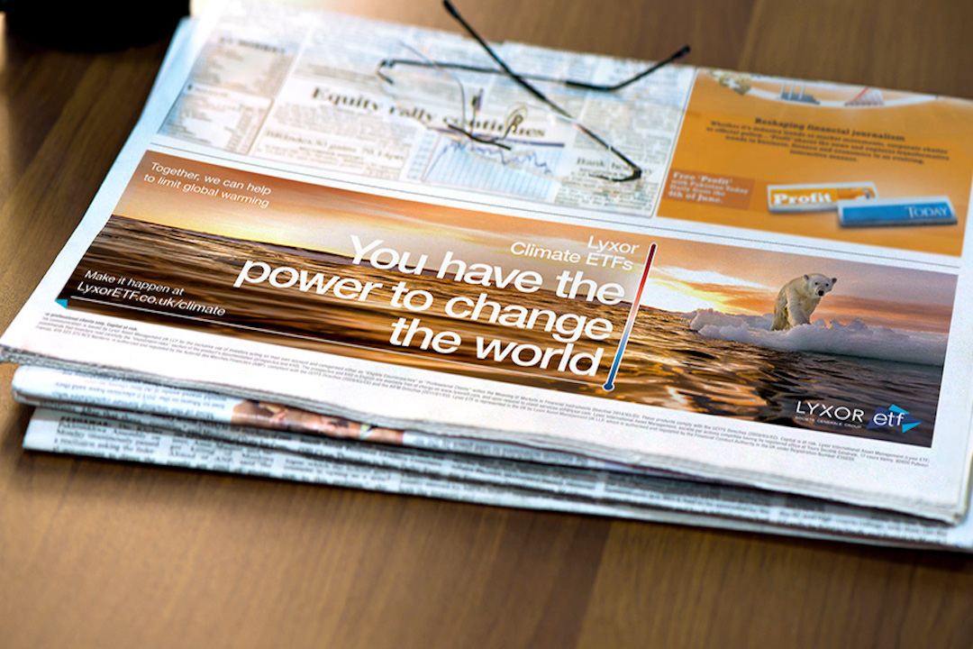 A newspaper on a table features an ad with a polar bear on melting ice, reading “You have the power to change the world!”—a Lyxor ETF case study promoting Climate ETFs and addressing global warming. Glasses rest atop the paper.