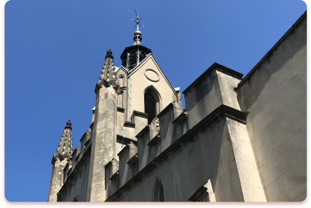 A stone church with gothic-style architecture, pointed arches, and a tall steeple rises against a clear blue sky, resembling a contact collider of history and faith.