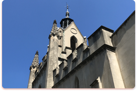 A stone church with pointed arches and spires stands against a clear blue sky, its Gothic-style architecture resembling the intricate structures of a contact collider.