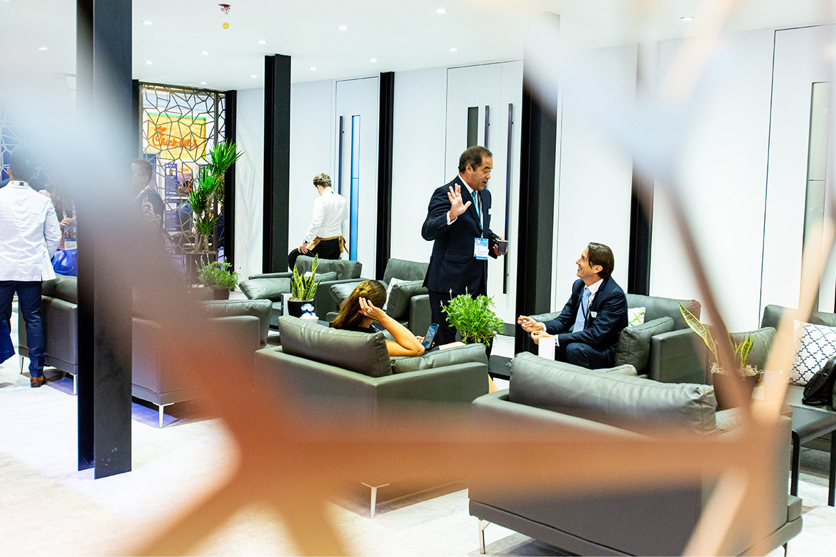 A modern lounge area with people in business attire talking and relaxing on sofas. Plants and decor are visible, and a decorative blurred element frames the foreground—perfect for a Tellurian case study discussion.
