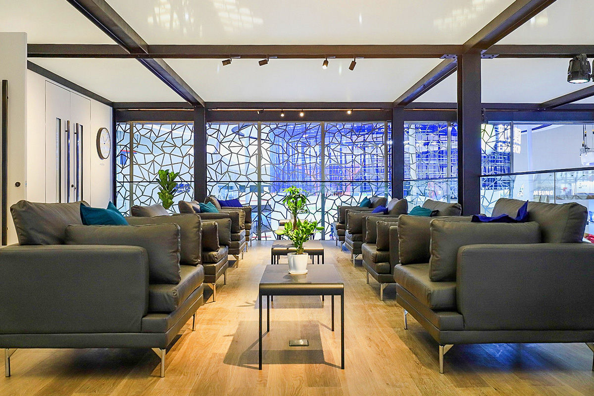 Modern lounge area with black leather armchairs, small tables with potted plants, wooden flooring, and a patterned glass wall letting in natural light. The spacious and inviting design echoes elements from the Tellurian case study.