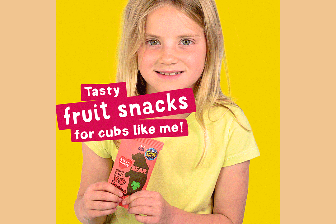 A young girl in a yellow shirt smiles while holding a Bear Fruit Yoyo snack packet. Bold text reads, Tasty fruit snacks for cubs like me! on a bright yellow background, inspired by our Bear Nibbles case study.
