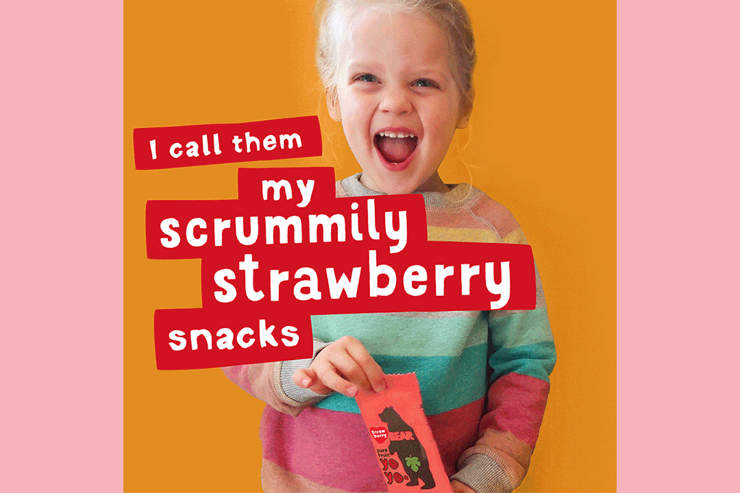 A smiling young girl in a striped sweater holds a pink snack packet against an orange background. Bold text reads, I call them my scrummily strawberry snacks, just like in our Bear Nibbles case study.