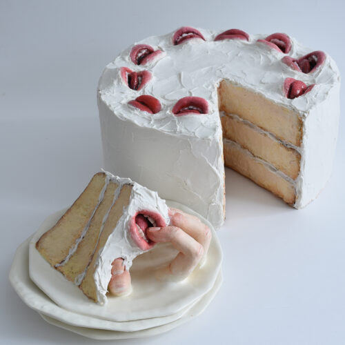 A three-layer white frosted cake with realistic mouths on top; a slice is cut out, and inside the slice, a sculpted human hand—like a creative marketing team reveal—emerges, holding the piece on a stack of plates.