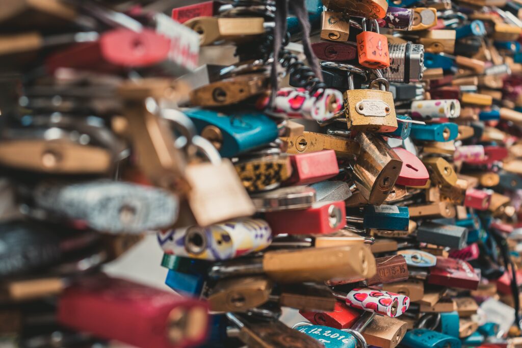 Close-up of dozens of colorful padlocks attached to metal cables, some with inscriptions or designs—these love locks symbolize commitment and are often used in experiential marketing campaigns on bridges or fences in various cities.