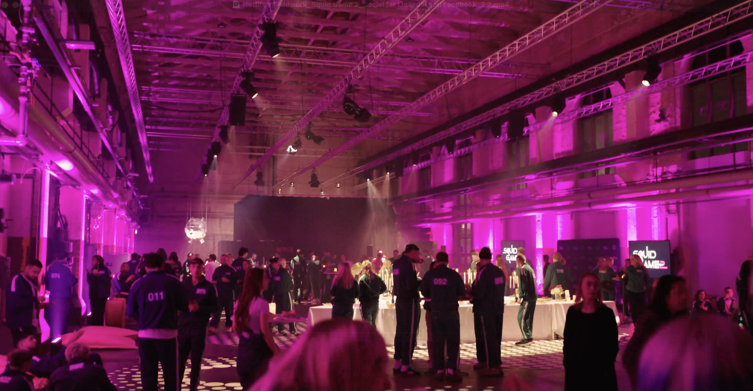 Large indoor event space filled with people socializing under vibrant pink and purple lighting, with high ceilings, visible beams, and tables scattered throughout the room—ideal for gatherings or trying out new activation tips.