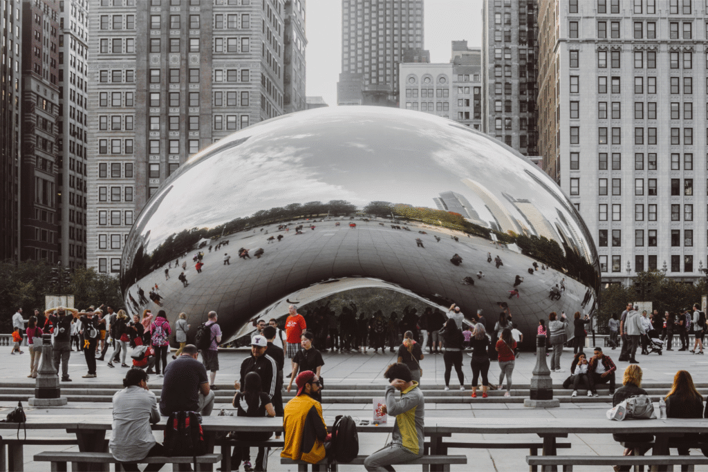 Crowds gather around the reflective Cloud Gate sculpture, also known as “The Bean,” in Chicago’s Millennium Park, where city buildings and greenery are mirrored on its shiny surface—an iconic backdrop for unforgettable brand activation events.