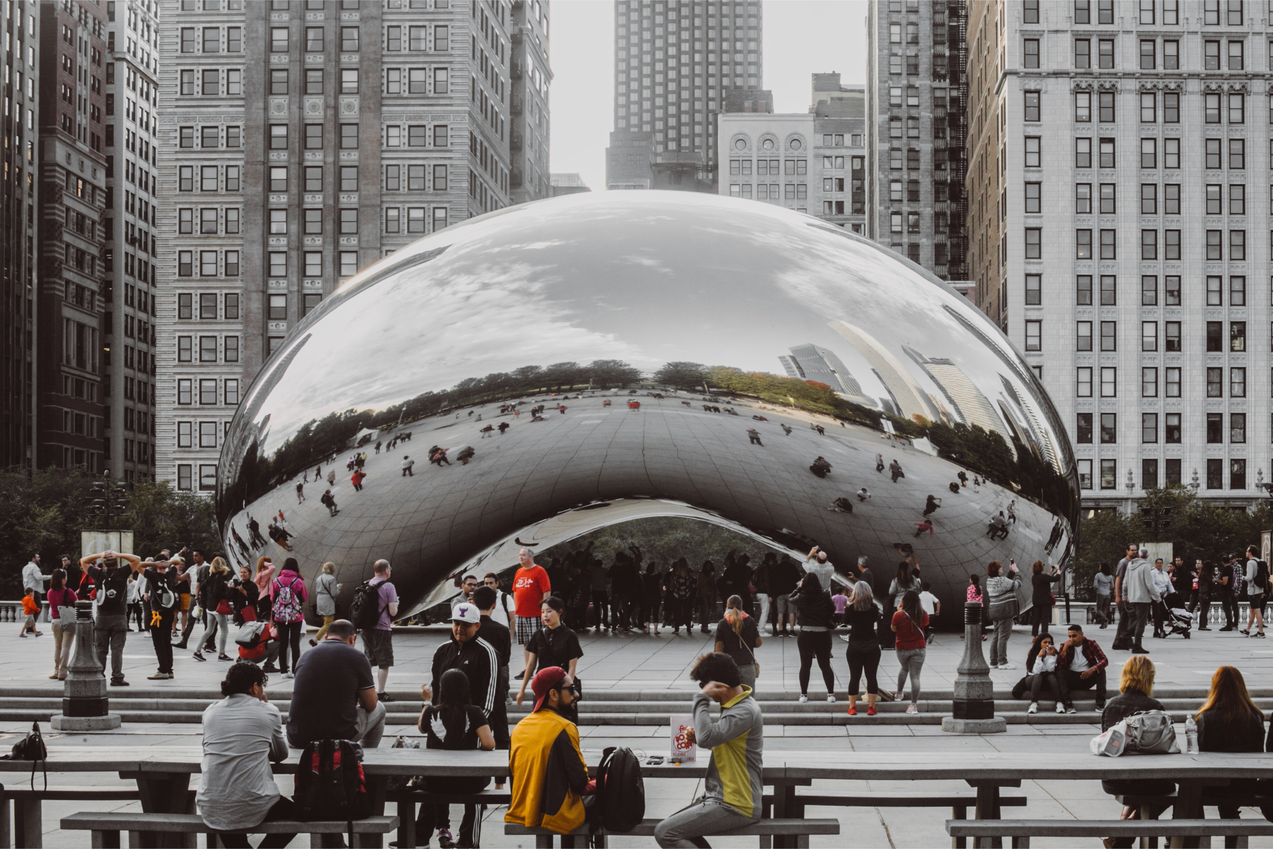 Crowds gather around the reflective Cloud Gate sculpture, also known as “The Bean,” in Chicago’s Millennium Park, where city buildings and greenery are mirrored on its shiny surface—an iconic backdrop for unforgettable brand activation events.
