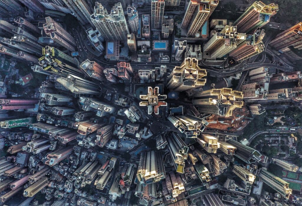 Aerial view of a dense cityscape with numerous tall skyscrapers clustered together, roads winding between the buildings, and patches of greenery visible around the edges.