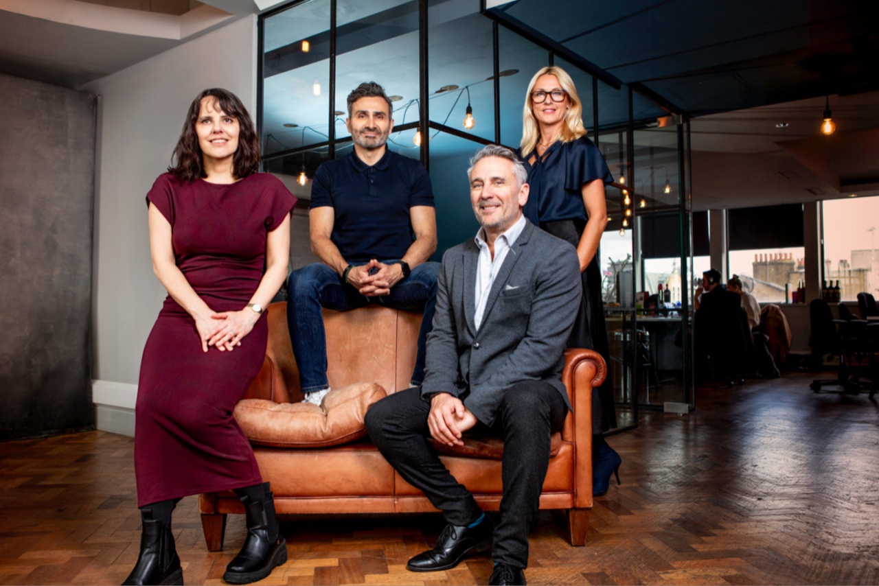 Portrait of four people in a room, corporate setting.